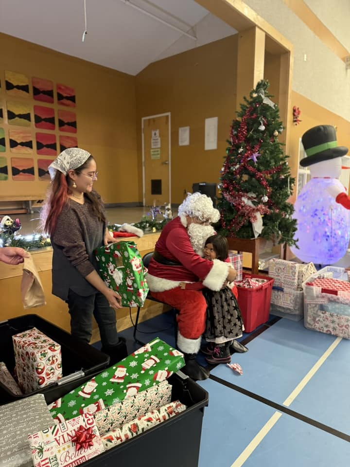 Santa Claus hugs a young girl while a woman holds a wrapped gift nearby
