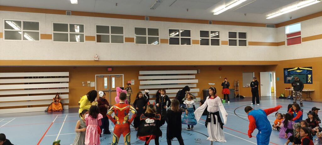 Children in various costumes dance together in a gym