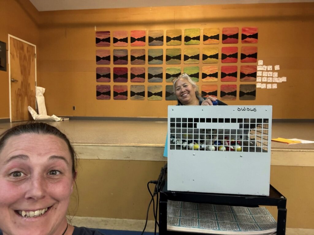 Two women smile at the camera, one holding a small caged storage unit filled with colorful items